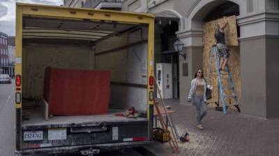 A woman walks past as Matt Harrington boards up a Vans shoe and apparel store near the French Quarter in New Orleans as tropical storm Barry approaches on July 11, 2019. - Tropical storm Barry barreled toward rain-soaked New Orleans on July 11 as the city hunkered down for an ordeal that evoked fearful memories of 2005's deadly Hurricane Katrina. (Photo by Seth HERALD / AFP)