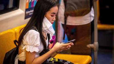 Una mujer usa su teléfono móvil después de quitarse la máscara protectora, usada entre los temores por la propagación del coronavirus COVID-19, en un tren aéreo suburbano en Bangkok el 13 de febrero de 2020. / AFP / Mladen ANTONOV