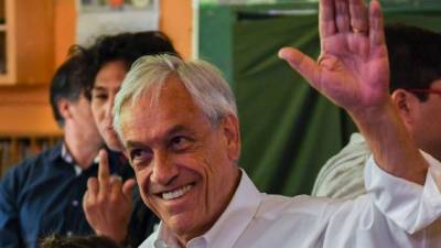 Chilean presidential candidate Sebastian Pinera waves after casting his vote as a young man (L) gestures besides him during the general election in Santiago on November 19, 2017. / AFP PHOTO / MARTIN BERNETTI