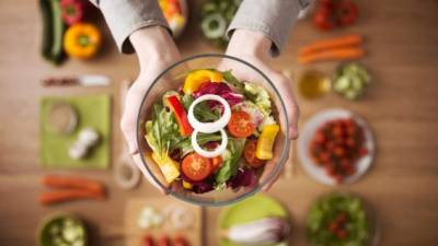 Hands holding an healthy fresh vegetarian salad in a bowl, fresh raw vegetables on background, top view