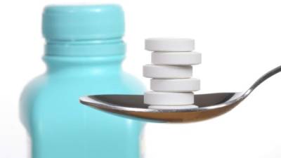 Antacid tablets on a spoon, a bottle of antacid blurred in the background