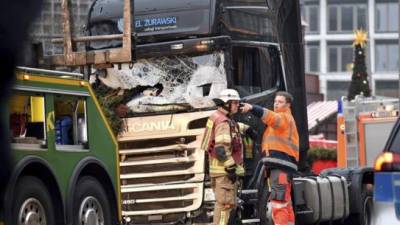 El trabajador de una compañía de remolque habla con un bombero antes de retirar el camión (d) que arrolló ayer a los visitantes de un mercadillo navideño en el centro de Berlín, donde murieron doce personas. EFE
