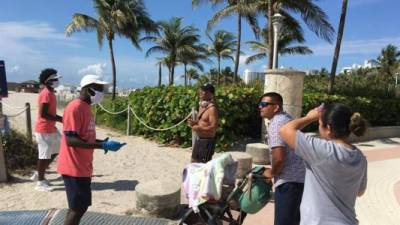 Unos jóvenes revisan las máscaras de unas personas a su llegada este miércoles a la playa de Miami Beach, Florida. EFE/Ivonne Malaver