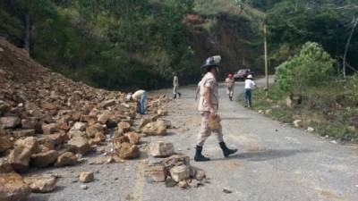 Un bombero camina por la carretera pavimentada en San Juancito del Distrito Central que se vio afectada por un derrumbe de rocas y arena.