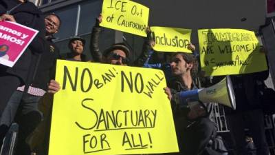 FILE - In this April 14, 2017, file photo, protesters hold up signs outside a courthouse where a federal judge was to hear arguments in the first lawsuit challenging President Donald Trump's executive order to withhold funding from communities that limit cooperation with immigration authorities in San Francisco. A federal judge Monday, Nov. 20, 2017, has permanently blocked President Donald Trump's executive order to cut funding from cities that limit cooperation with U.S. immigration authorities. San Francisco and Santa Clara County had filed lawsuits. (AP Photo/Haven Daley, File)