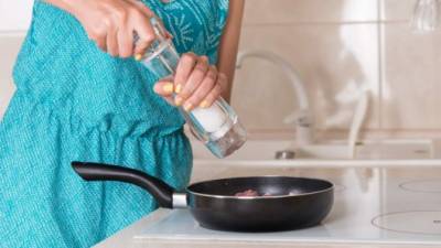 Woman grinding salt from a salt mill into a frying pan as she cooks the dinner, close up of her hands and the pan