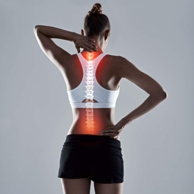 Studio shot of an athletic young woman holding her neck and back in pain against a grey background