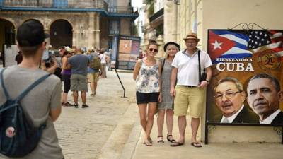 Turistas posan junto a un cartel que representa el acercamiento entre Cuba y Estados Unidos, a la entrada de un restaurante en La Habana.