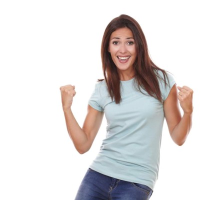 Portrait of charming adult woman on blue t-shirt and blue jeans celebrating her victory while smiling at you with funny face and standing on isolated studio