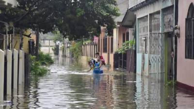 Dos jóvenes hondureños abandonan sus viviendas inundadas debido a las fuertes lluvias hoy en La Lima.