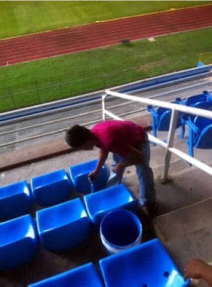 Un trabajador pintando las sillas del estadio Olímpico de color azul.