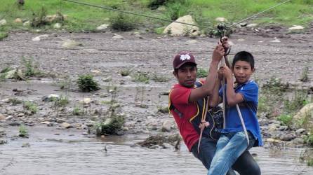 Un hombre y un menor en el momento que cruzan el río por un cable de acero.