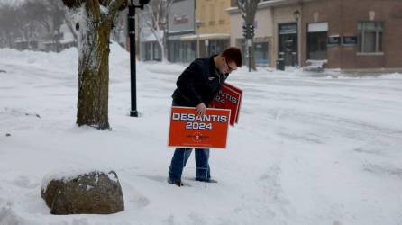 Una persona coloca carteles de campaña del candidato presidencial republicano, el gobernador de Florida, Ron DeSantis, afuera del edificio donde realiza una parada de campaña el 13 de enero de 2024.