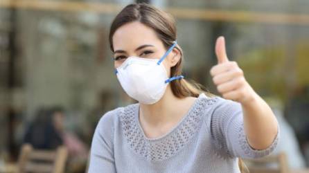 Woman doing thumbs up gesture wearing a protective mask avoiding contagion on a terrace