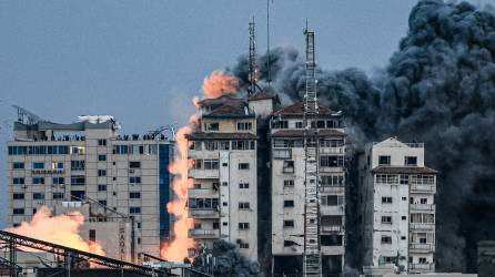 Personas paradas en una azotea observan cómo una bola de fuego y humo se eleva sobre un edificio en la ciudad de Gaza el 7 de octubre de 2023 durante un ataque aéreo israelí.