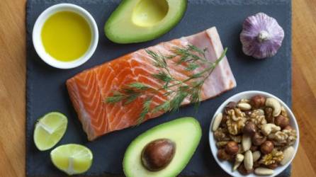Table top still life of foods high in healthy fats such as olive oil, Salmon, nuts and avocados with vegetables and herbs.