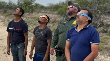 Agente fronterizo de Estados Unidos junto a migrantes observando el paso del eclipse solar.