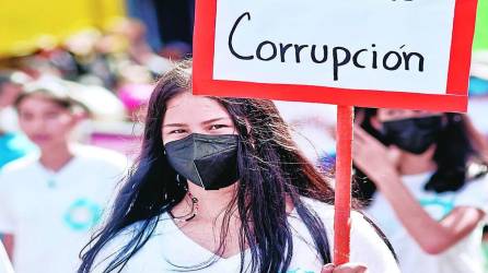 Joven hondureña sostiene un letrero con el mensaje “No más corrupción” en una protesta.