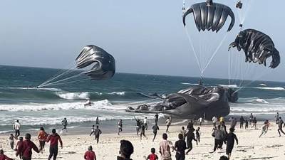 Gazatíes reciben la ayuda humanitaria lanzada en paracaídas.