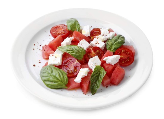 Salad with watermelon, feta and basil leaves on plate, isolated on white