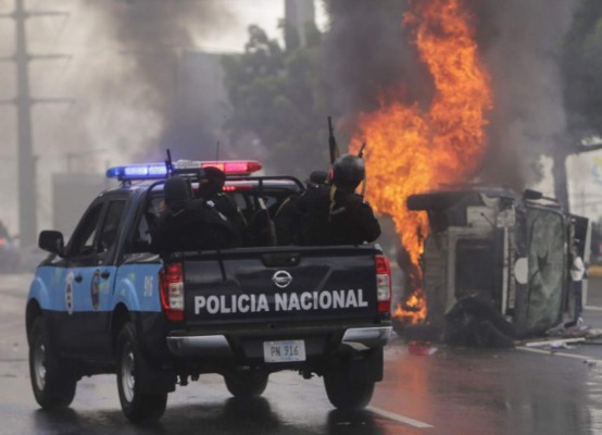 National Police officers in riot gear, drive near an overturned burning police vehicle, after an anti-government protest in Managua, on September 2, 2018. At least two people were injured on Sunday, when alleged paramilitaries fired against an opposition march, which ended up in violence in eastern Managua. / AFP PHOTO / INTI OCON