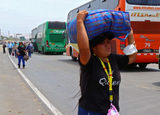 A woman carries luggage as the Pan-American road remains blocked near Viru, Peru on December 3, 2020, during a peasants protest to demand labour reforms, better wages and other benefits for workers of the agricultural sector, joining a similar protest going on in the south of the country. - A rural worker was killed Thursday in Peru after being shot while police tried to clear a roadblock, in the first labour conflict under the government of President Francisco Sagasti. (Photo by Celso ROLDAN / AFP)