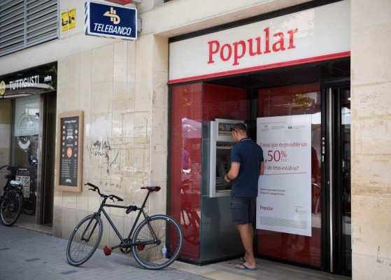 A man operates at the ATM at a Banco Popular branch on June 7, 2017 in Vilanova i la Geltru near Barcelona after European authorities announced the sale of Spain's Banco Popular to compatriot Banco Santander to avert a looming failure of the troubled lender in a solution that will not leave Spanish taxpayers to pick up the tab. / AFP PHOTO / LLUIS GENE