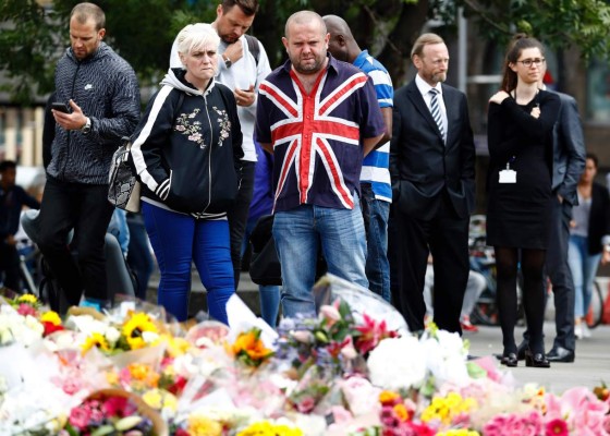 A man wearing a Union Flag-themed shirt looks at flowers placed at the south side of London Bridge, close to Borough Market in London on June 5, 2017, in tribute to the victims of the June 3 attacks.British police on Monday made several arrests in two dawn raids following the June 3 London attacks, claimed by the Islamic State group which left seven people dead. / AFP PHOTO / Odd ANDERSEN