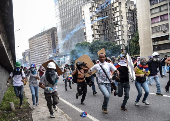 Venezuelan opposition activists run from clashes with the security forces during a protest march against the government of Nicolas Maduro in Caracas on May 13, 2017.Daily clashes between demonstrators -who blame elected President Nicolas Maduro for an economic crisis that has caused food shortages- and security forces have left 38 people dead since April 1. Protesters demand early elections, accusing Maduro of repressing protesters and trying to install a dictatorship. / AFP PHOTO / JUAN BARRETO