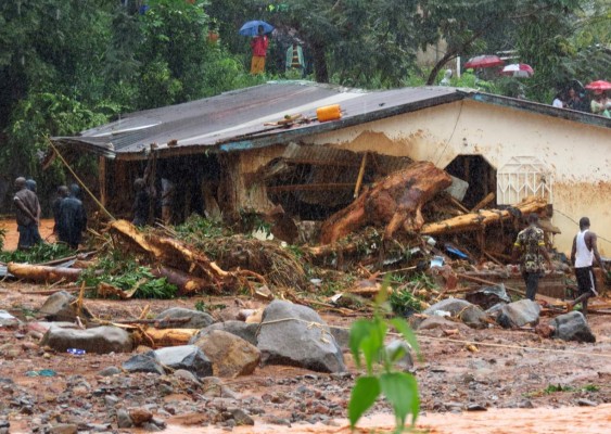 TOPSHOT - Bystanders and rescue personnel gather beside a flood damaged building in an area of Freetown on August 14, 2017, after landslides struck the capital of the west African state of Sierra Leone. At least 312 people were killed and more than 2,000 left homeless when heavy flooding hit Sierra Leone's capital of Freetown, leaving morgues overflowing and residents desperately searching for loved ones. An AFP journalist at the scene saw bodies being carried away and houses submerged in two areas of the city, where roads turned into churning rivers of mud and corpses were washed up on the streets. / AFP PHOTO / SAIDU BAH