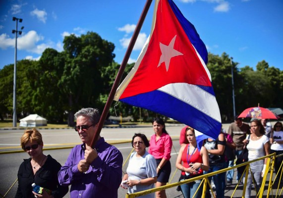 People holding a Cuban national flag queue to enter Jose Marti's memorial to pay their last respects to Cuban revolutionary icon Fidel Castro at Revolution Square in Havana, on November 28, 2016. A titan of the 20th century who beat the odds to endure into the 21st, Castro died late Friday after surviving 11 US administrations and hundreds of assassination attempts. No cause of death was given. Castro's ashes will go on a four-day island-wide procession starting Wednesday before being buried in the southeastern city of Santiago de Cuba on December 4. / AFP PHOTO / RONALDO SCHEMIDT