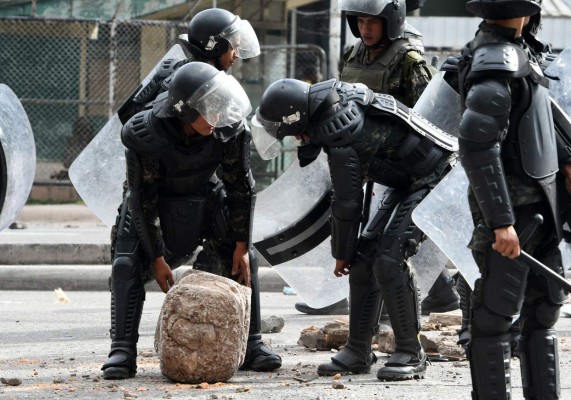 Honduran riot police members clear stones and rocks from the Comunidad Economica Europea boulevard, blocked by high school students demanding the resignation of President Juan Orlando Hernandez, in Tegucigalpa, on June 25, 2019. - Ongoing protests against Hernandez -which started more than a month ago called by doctors and teachers against health and education laws- intensified last week when three people were killed. On the eve, Honduran military police opened fire on protesting students at a university, wounding at least five, according to campus and hospital officials. (Photo by ORLANDO SIERRA / AFP)