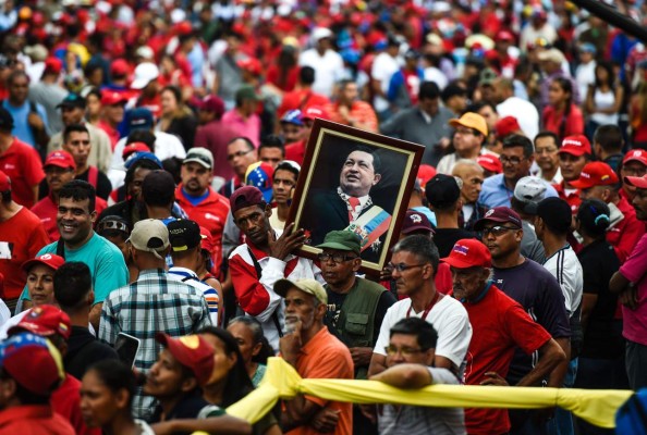 Supporters of Venenzuelan president Nicolas Maduro hold a portrait of late Venezuelan President Hugo Chavez during a rally in Caracas on August 27, 2016. / AFP PHOTO / JUAN BARRETO