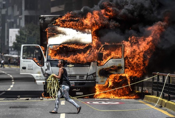 TOPSHOT - A truck set ablaze by opposition activists blocking an avenue during a protest burns in Caracas, on July 18, 2017. The Venezuelan opposition called for a 24-hour national civic strike next Thursday to pressure President Nicolas Maduro to withdraw the call to a National Constituent Assembly, after achieving a massive vote of rejection in a symbolic plebiscite. / AFP PHOTO / JUAN BARRETO