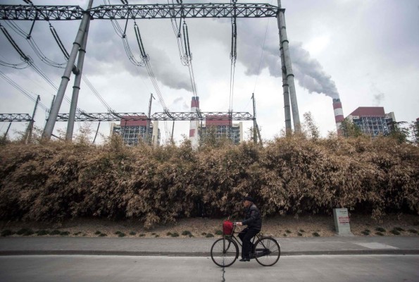 This file photo taken on March 22, 2016 shows a man passing the Shanghai Waigaoqiao Power Generator Company coal power plant in Shanghai. - UN chief Antonio Guterres on Saturday, December 12, urged world leaders to declare a 'state of climate emergency' and shape greener growth after the coronavirus pandemic, as he opened a summit marking five years since the landmark Paris Agreement. (Photo by JOHANNES EISELE / AFP) / XGTY