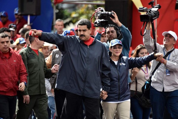 Venezuelan President Nicolas Maduro (L) and his wife Cilia Flores wave at supporters during a rally on May Day in Caracas, on May 1, 2017.Security forces in Venezuela fired tear gas to drive back protesters Monday as pro- and anti-government May Day rallies erupted exactly one month into a wave of deadly political unrest. Officers clashed with some 300 protesters, some throwing stones, who tried to break through security barriers to the electoral council headquarters in central Caracas. / AFP PHOTO / Carlos BECERRA