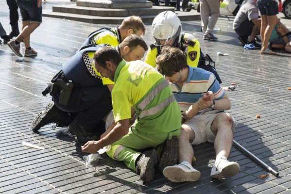 A person is helped by Spanish policemen and two men after a van ploughed into the crowd, killing at least 13 people and injuring around 100 others on the Rambla in Barcelona on August 17, 2017.A driver deliberately rammed a van into a crowd on Barcelona's most popular street on August 17, 2017 killing at least 13 people before fleeing to a nearby bar, police said. Officers in Spain's second-largest city said the ramming on Las Ramblas was a 'terrorist attack'. The driver of a van that mowed into a packed street in Barcelona is still on the run, Spanish police said. / AFP PHOTO / Nicolas CARVALHO OCHOA
