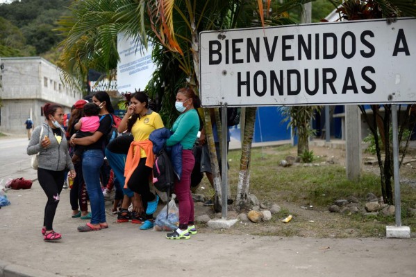 Honduran migrant Rosa Baquenado (R), who voluntarely returns to her country, is seen alongside other migrants next to a sign reading Welcome to Honduras in El Florido, Chiquimula, Guatemala on January 19, 2021. - On buses and trucks, Guatemala transported Tuesday several groups of migrants who were part of a US-bound caravan back to Honduras, after police and military officers forced them to desist from the crossing. (Photo by Johan ORDONEZ / AFP)