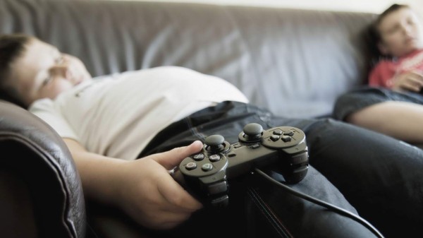 Two boys sleeping on sofa while holding games consoles