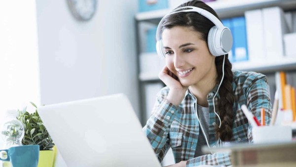 Teenage smiling girl using a laptop and wearing headphones, technology and leisure concept