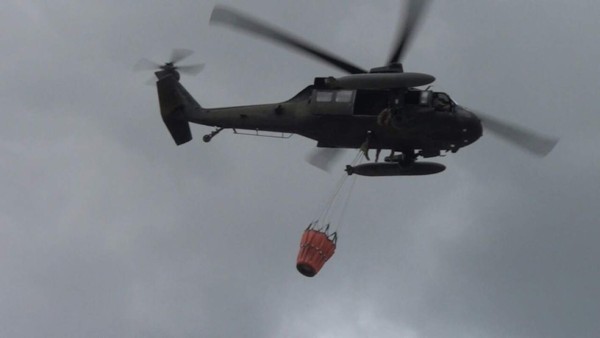 Un helicóptero de las Fuerzas Armadas cargado de agua sobrevuela la zona del incendio.