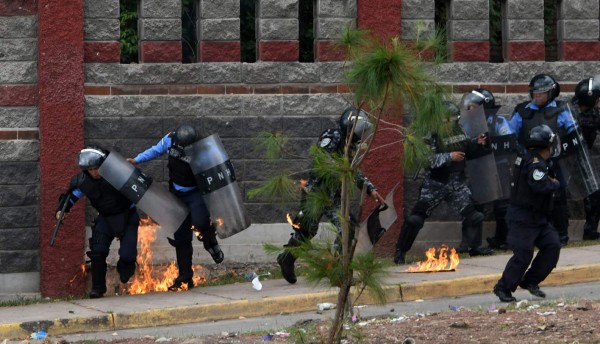 Riot police officers and members of the Cobra Special Unit trying to disperse students of the National Autonomous University of Honduras (UNAH) gathered under the University Student Movement (MEU) who were blocking a boulevard to demand, among other things, the resignation of rector Julieta Castellanos, are hit with a Molotov cocktail during clashes in Tegucigalpa, on July 25, 2017.The MEU, who is occupying several buildings of the UNAH since June 13 preventing some 50,000 students from attending classes, also demands the cessation of the 'criminalization' of protests, the suspension of student hearings and support to appoint delegates to the University Council, UNAH's main decision-making body. / AFP PHOTO / Orlando SIERRA