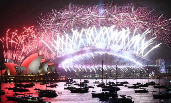 TOPSHOT - New Year's Eve fireworks erupt over Sydney's iconic Harbour Bridge and Opera House (L) during the fireworks show on January 1, 2020. (Photo by PETER PARKS / AFP)