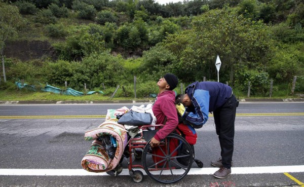 Venezuelan migrant Jefferson Alexis and his father Jose Agustin Lopez, in a wheelchair, stop to rest as they travel along the road linking Cucuta and Pamplona, in Norte de Santander Department, Colombia, on September 15, 2018.Lopez started an odyssey to Bogota looking for the medicines he could not gey in Venezuela. / AFP PHOTO / SCHNEYDER MENDOZA