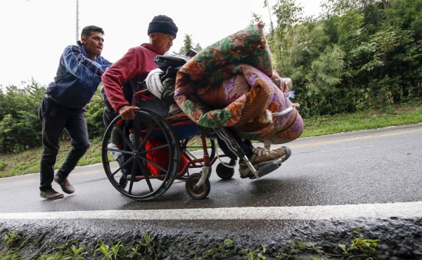 Venezuelan migrant Jefferson Alexis pushes his father Jose Agustin Lopez's wheelchair along the road linking Cucuta and Pamplona, in Norte de Santander Department, Colombia, on September 15, 2018.Lopez started an odyssey to Bogota looking for the medicines he could not gey in Venezuela. / AFP PHOTO / SCHNEYDER MENDOZA