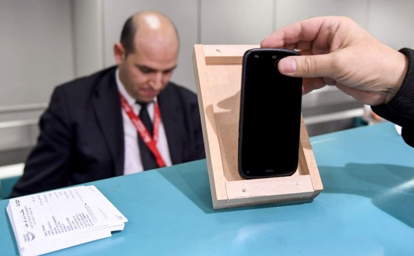 A Tunisian traveller measures the size of his cell phone in a frame on the check-in counter to be cleared for boarding his London-bound flight at Tunis-Carthage International Airport, on March 25, 2017.The United States this week announced a ban on all electronics larger than a standard smartphone on board direct flights out of eight countries across the Middle East, in effect from March 25, 2017. US officials would not specify how long the ban will last, but Emirates told AFP that it had been instructed to enforce the measures until at least October 14. Britain has also announced a parallel electronics ban targeting all flights out of Egypt, Turkey, Jordan, Saudi Arabia, Tunisia and Lebanon. / AFP PHOTO / FETHI BELAID