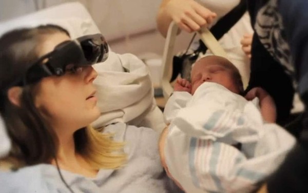 El momento cuando Kathy Beitz logra ver a su hijo recién nacido con la ayuda de unos lentes en un casco negro de gran tamaño. Foto AFP.