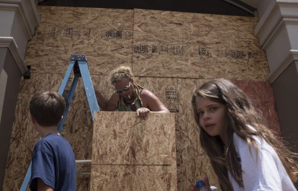 Kids walk past as Matt Harrington boards up a Vans shoe and apparel store near the French Quarter in New Orleans as tropical storm Barry approaches on July 11, 2019. - Tropical storm Barry barreled toward rain-soaked New Orleans on July 11 as the city hunkered down for an ordeal that evoked fearful memories of 2005's deadly Hurricane Katrina. (Photo by Seth HERALD / AFP)