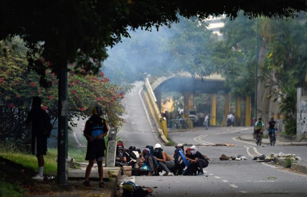 Opposition demonstrators take shelter during an anti-government protest in Caracas, on July 20, 2017.A 24-hour nationwide strike got underway in Venezuela Thursday, in a bid by the opposition to increase pressure on beleaguered leftist President Nicolas Maduro following four months of deadly street demonstrations. / AFP PHOTO / JUAN BARRETO