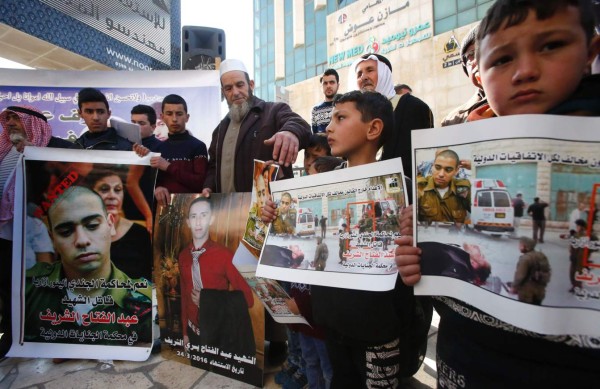 Palestinians holds placards during a demonstration following a verdict in the trial of the Israeli soldier Elor Azaria (portrait-L) who in March 2016 shot dead wounded alleged Palestinian assailant Abdul Fatah al-Sharif (portrait-C) as he lay on the ground, in the occupied West Bank city of Hebron, on February 21, 2017.Israeli Judge Maya Heller handed down the sentence a month after Elor Azaria, 21, was found guilty of manslaughter for killing Palestinian Abdul Fatah al-Sharif as he lay on the ground in the southern occupied West Bank. / AFP PHOTO / HAZEM BADER